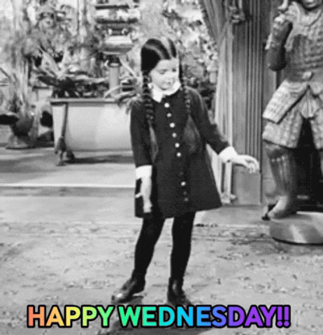 TV gif. In black and white, Wednesday Addams from the original Addams Family dances in her house. She has a happy, but concentrated look on her face as she does a little two step and wiggle of the arms. The rainbow flashing text at the bottom says, “Happy Wednesday!!”