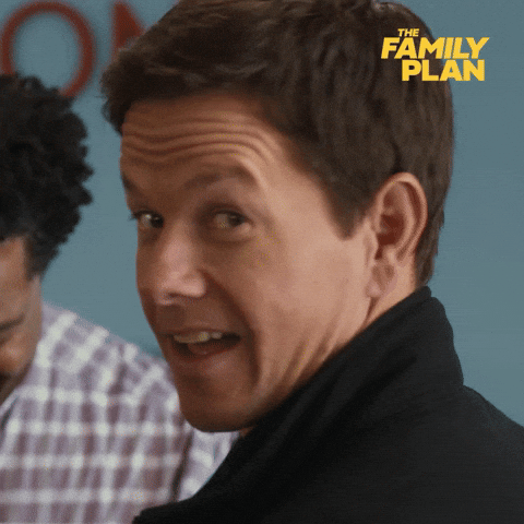 Movie gif. Mark Wahlberg as Dale in "The Family Plan" turns to look back over his shoulder at us with a sarcastic smirk on his face and gives a quick wink.